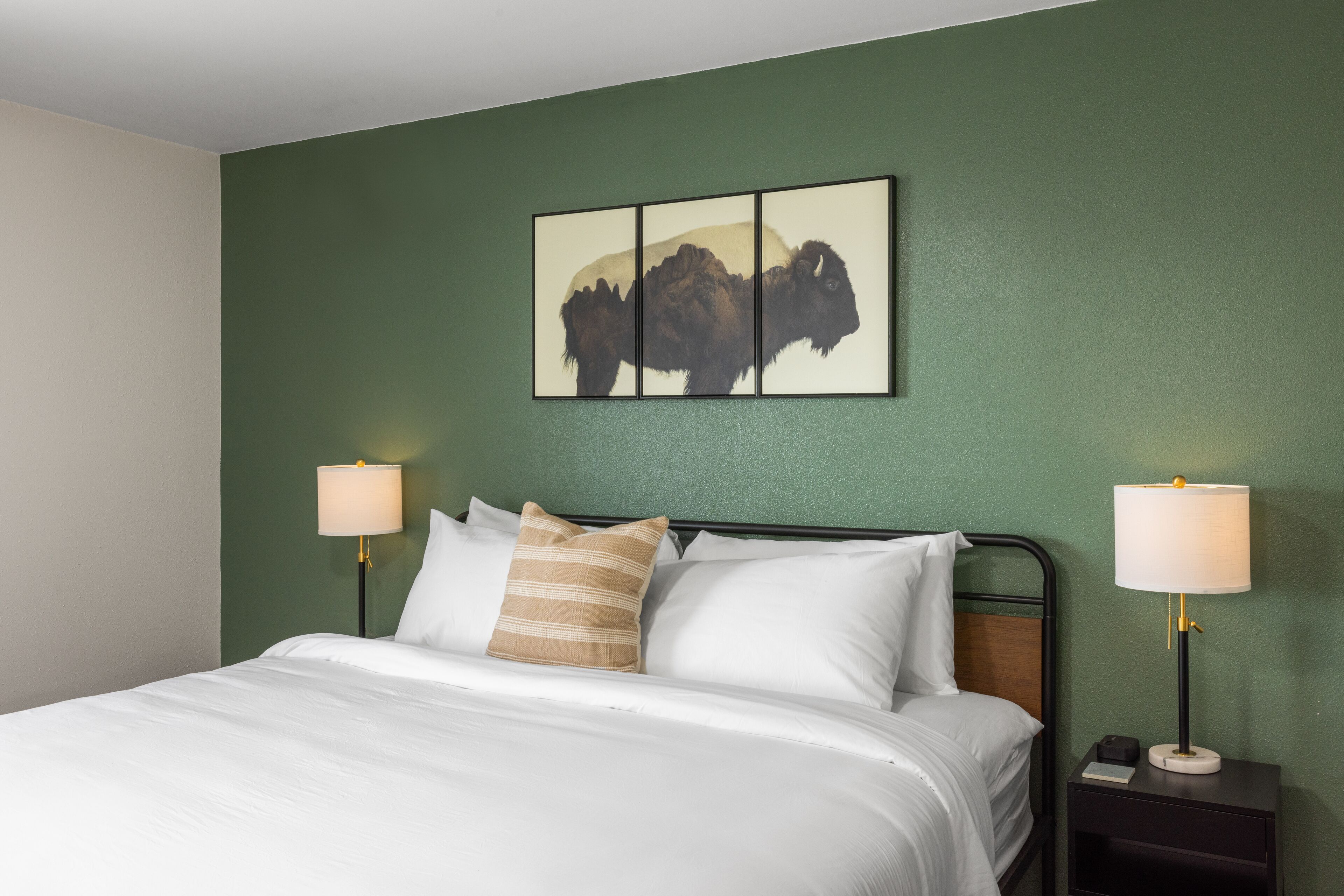Uma cama bem arrumada com lençóis brancos, parede verde e uma obra de arte emoldurada acima.