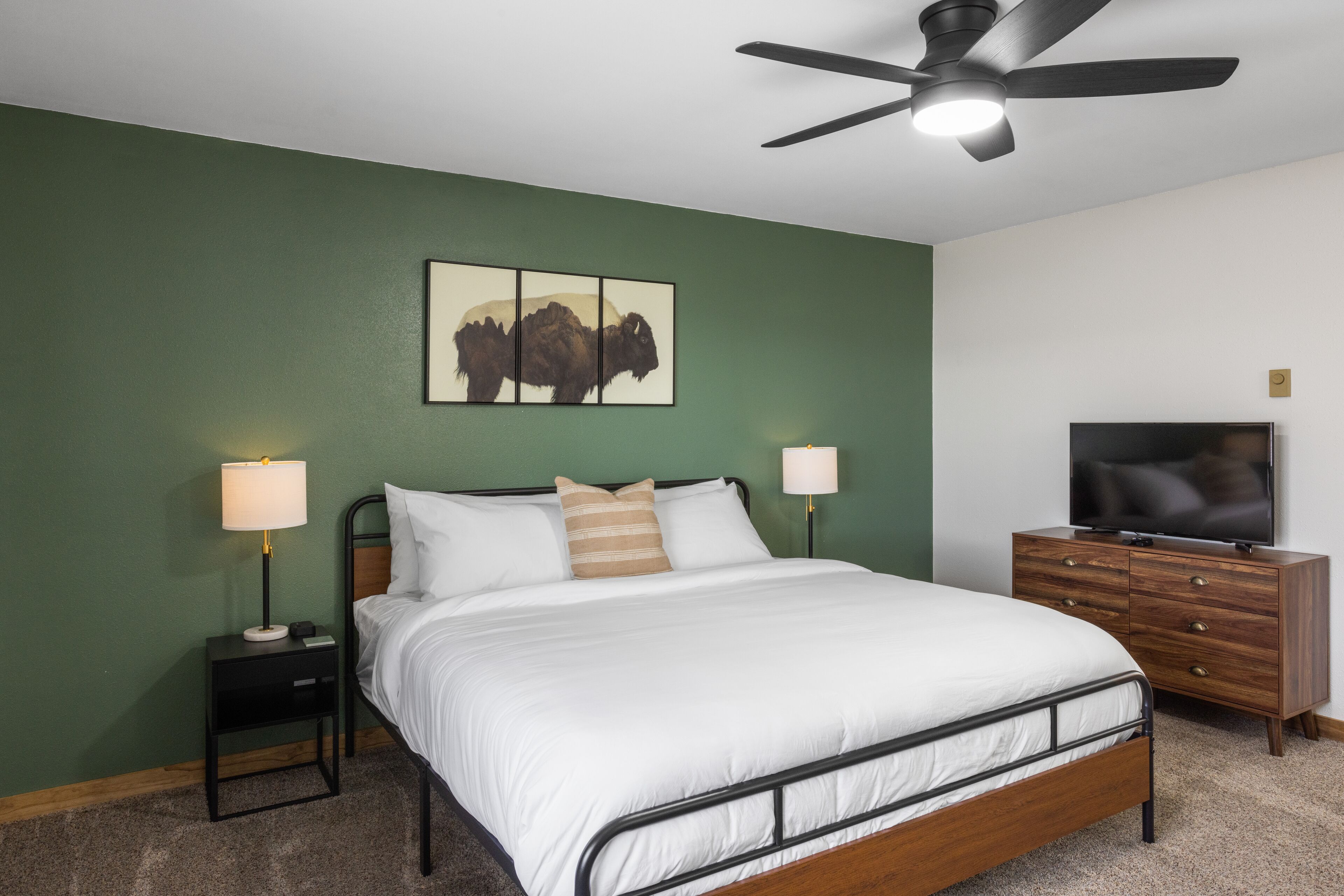 A bedroom with a bed, nightstands, a TV, and a ceiling fan.