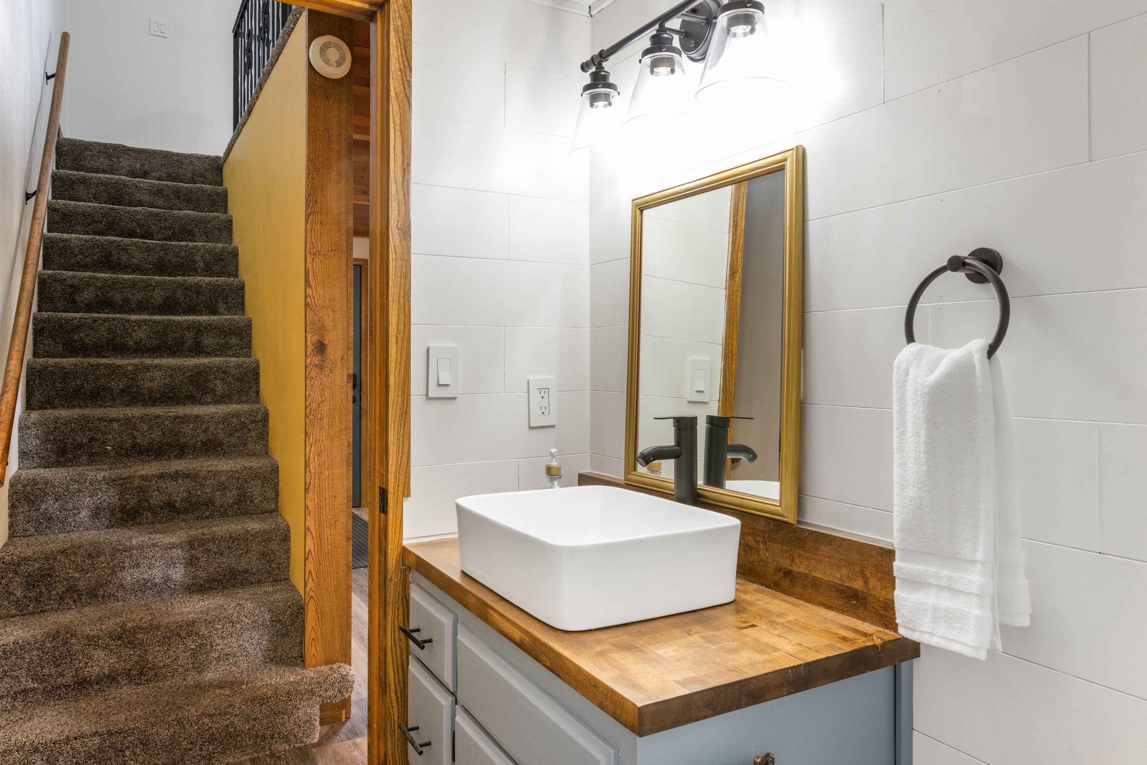 A bathroom with a wooden staircase, a white sink, a mirror, and a towel rack.