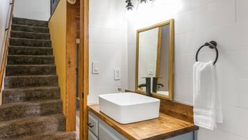 A bathroom with a wooden staircase, a white sink, a mirror, and a towel rack.