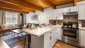 A modern kitchen with white cabinets, a stainless steel stove, and a marble countertop. - Otters Den (West Yellowstone)