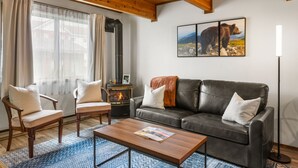 A cozy living room with a fireplace, leather sofa, wooden chairs, and a coffee table. - Otters Den (West Yellowstone)
