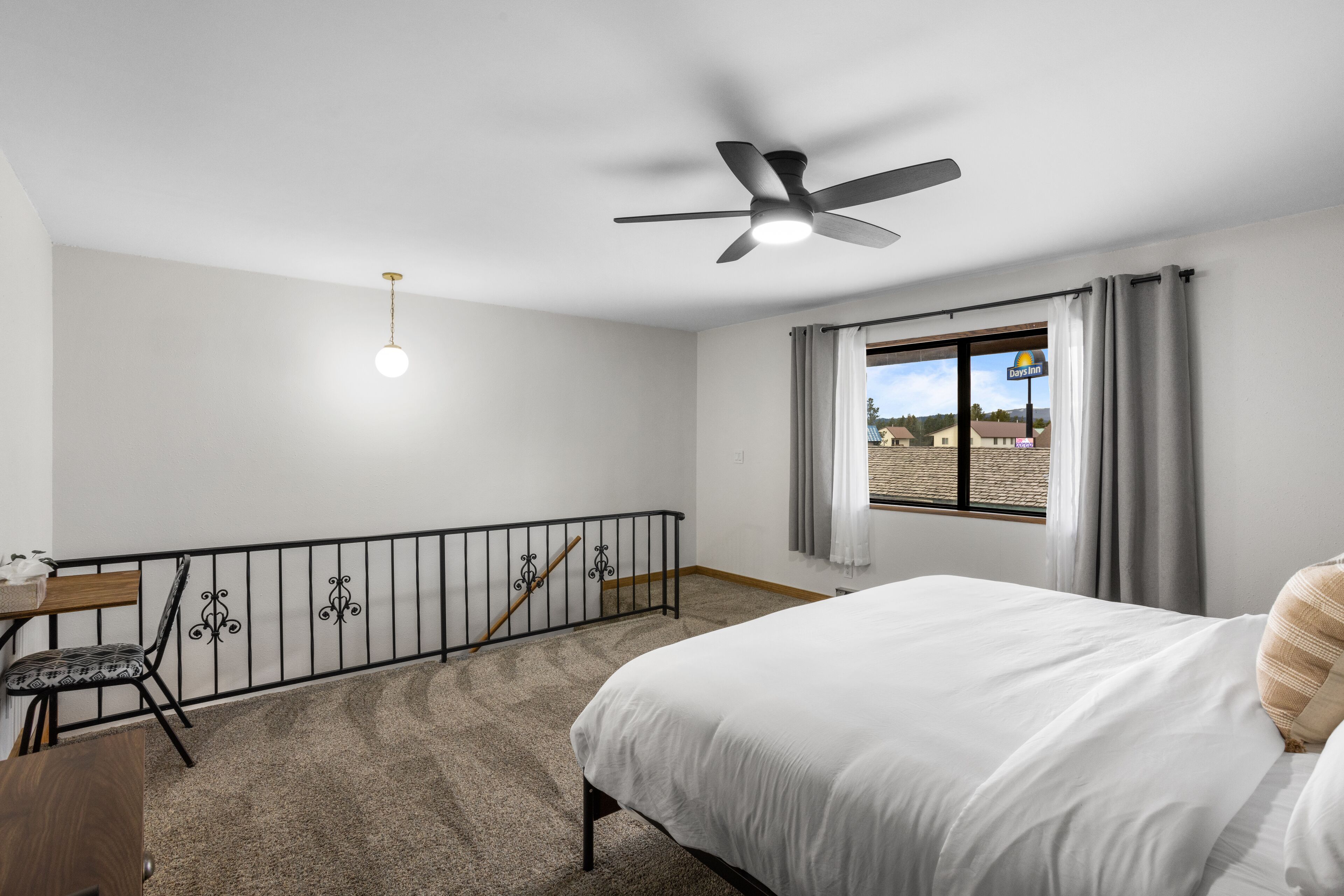 Une chambre à coucher comprenant un lit, un bureau, une chaise, un ventilateur de plafond et une fenêtre avec des rideaux.