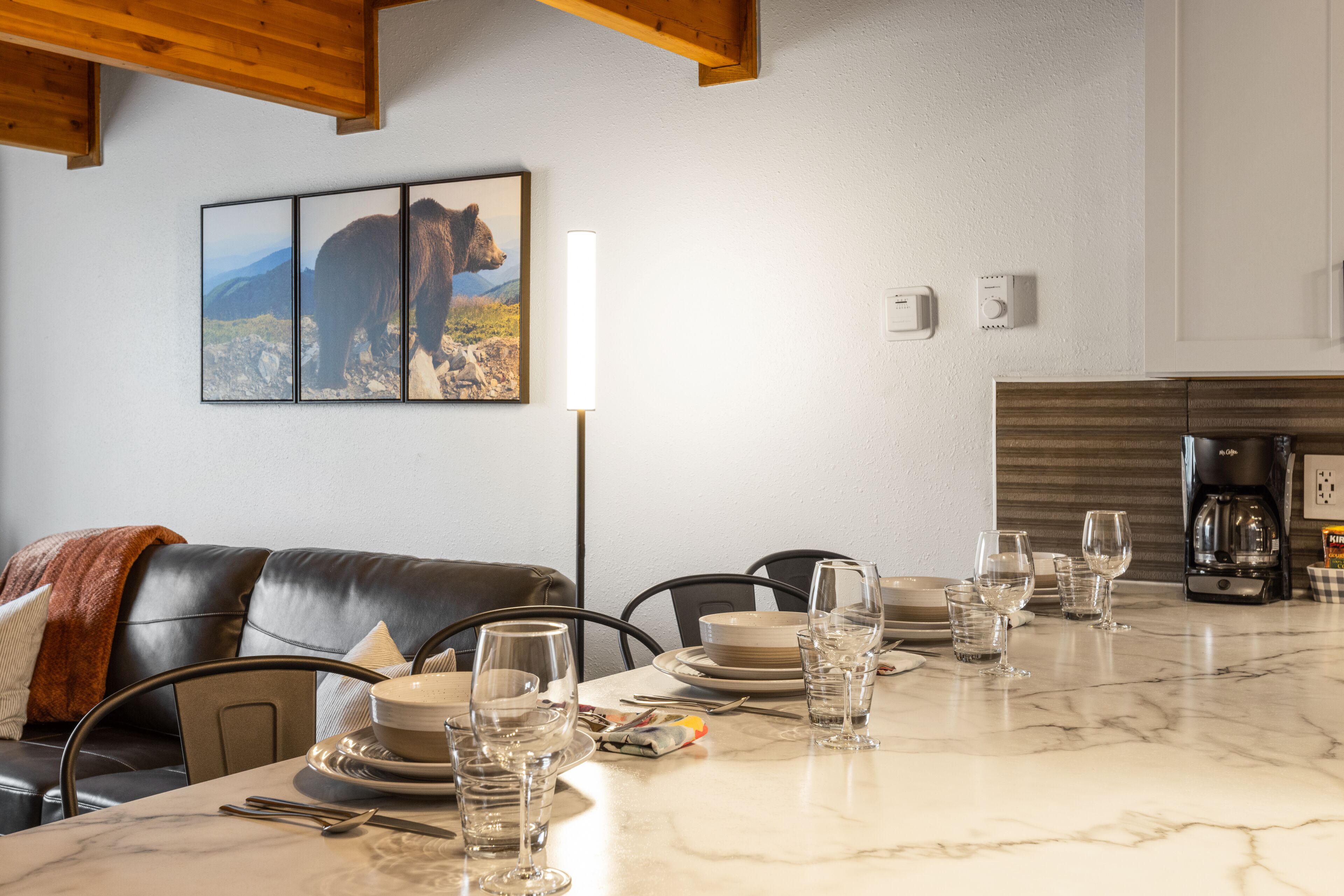 A dining area with a marble table set for six, a leather couch, and a bear-themed artwork on the wall.