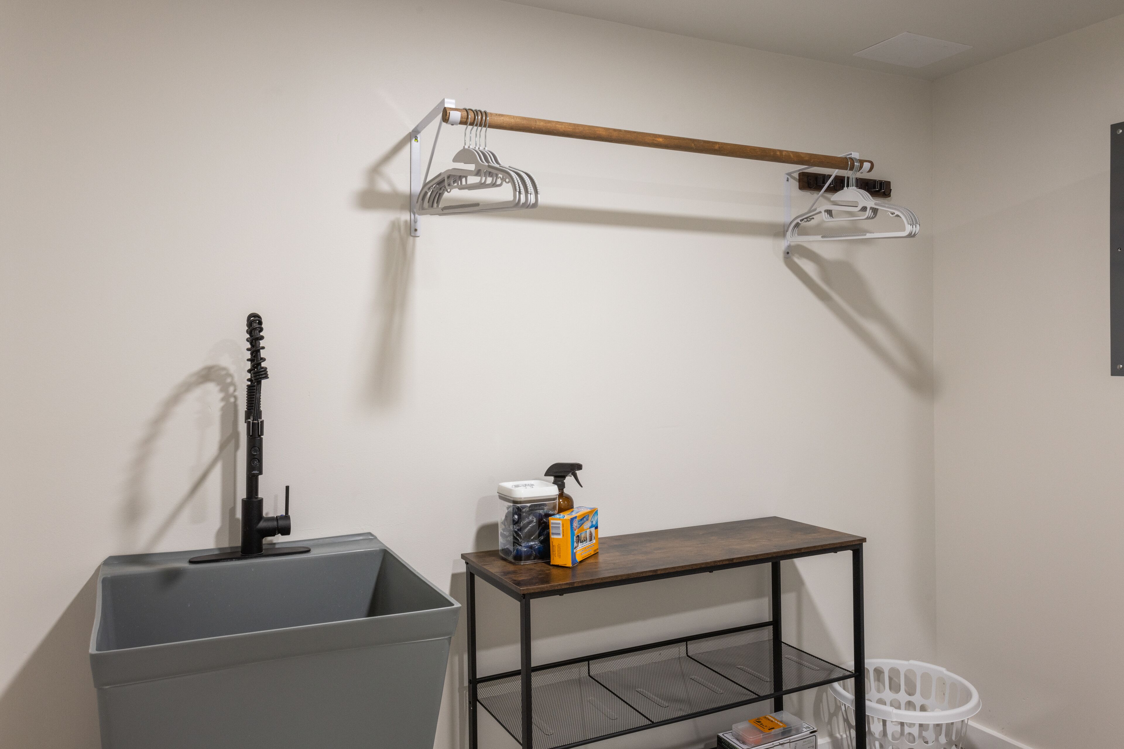 A laundry area with a washing machine, a drying rack, a metal shelf, and a trash bin.