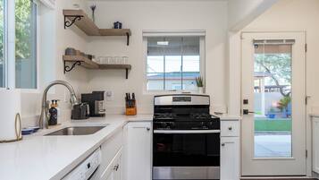 Una cocina con armarios blancos, una estufa de acero inoxidable y ventana con vista a un patio trasero.