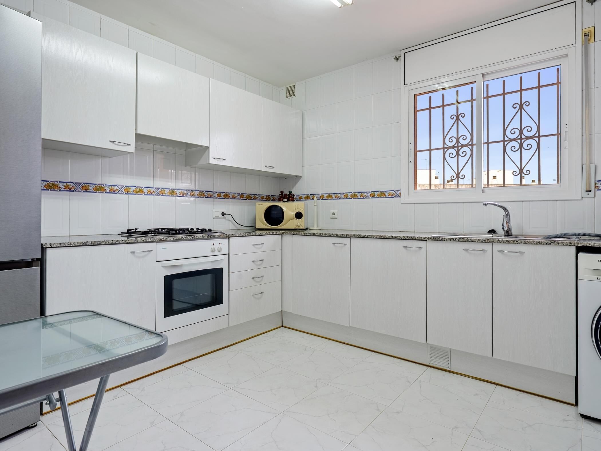 A kitchen with white cabinets, a stove, oven, microwave, and a window with decorative bars.