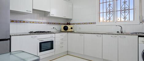 A kitchen with white cabinets, a stove, oven, microwave, and a window with decorative bars.