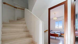 Un escalier menant à une chambre à coucher équipée d’un lit, d’une fenêtre et d’un luminaire suspendu.