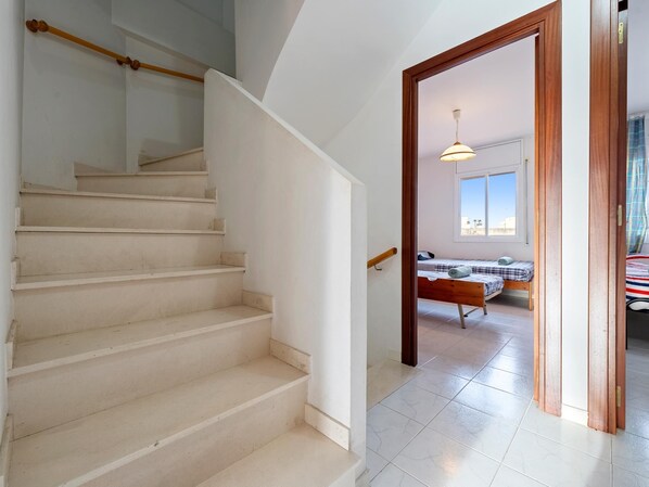 A staircase leading to a bedroom with a bed, a window, and a hanging light fixture.