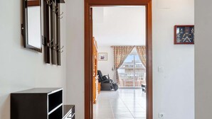 Un couloir menant à un balcon où se trouvent une trottinette, une armoire en bois et un tableau encadré accroché au mur.