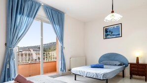 Une chambre à coucher avec un lit, une table de chevet, une lampe, une fenêtre avec des rideaux et une vue sur l’extérieur.