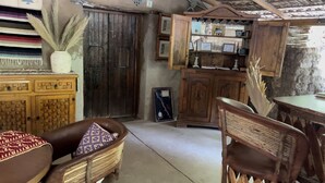 A rustic room with wooden furniture, a woven chair, a cabinet with framed pictures, and a decorative vase with dried plants. - Hacienda Ramona (Comondu)