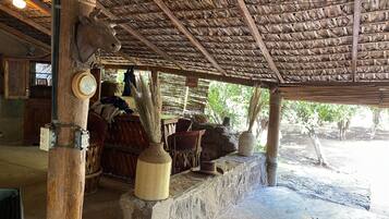 Una estructura rústica de madera con techo de paja, un armario de madera, una cesta de mimbre y una pared de piedra.