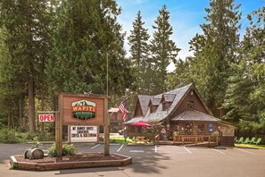 Een rustieke lodge met een bordje dat aangeeft dat het geopend is, een parkeerplaats en een picknicktafel.