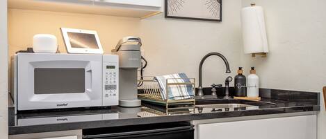 A compact kitchen with a microwave, coffee maker, and a dish rack.