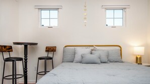 A bedroom with a bed, two windows, a table, two chairs, and a lamp.
