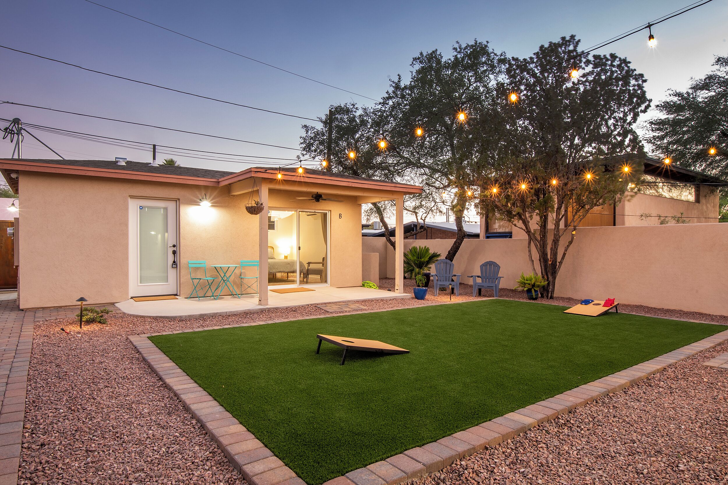 A backyard with artificial grass, a wooden bench, and a small house with a covered patio.