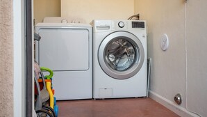 A laundry area with a front-loading washing machine and dryer, a small toy cart, and a doorbell.