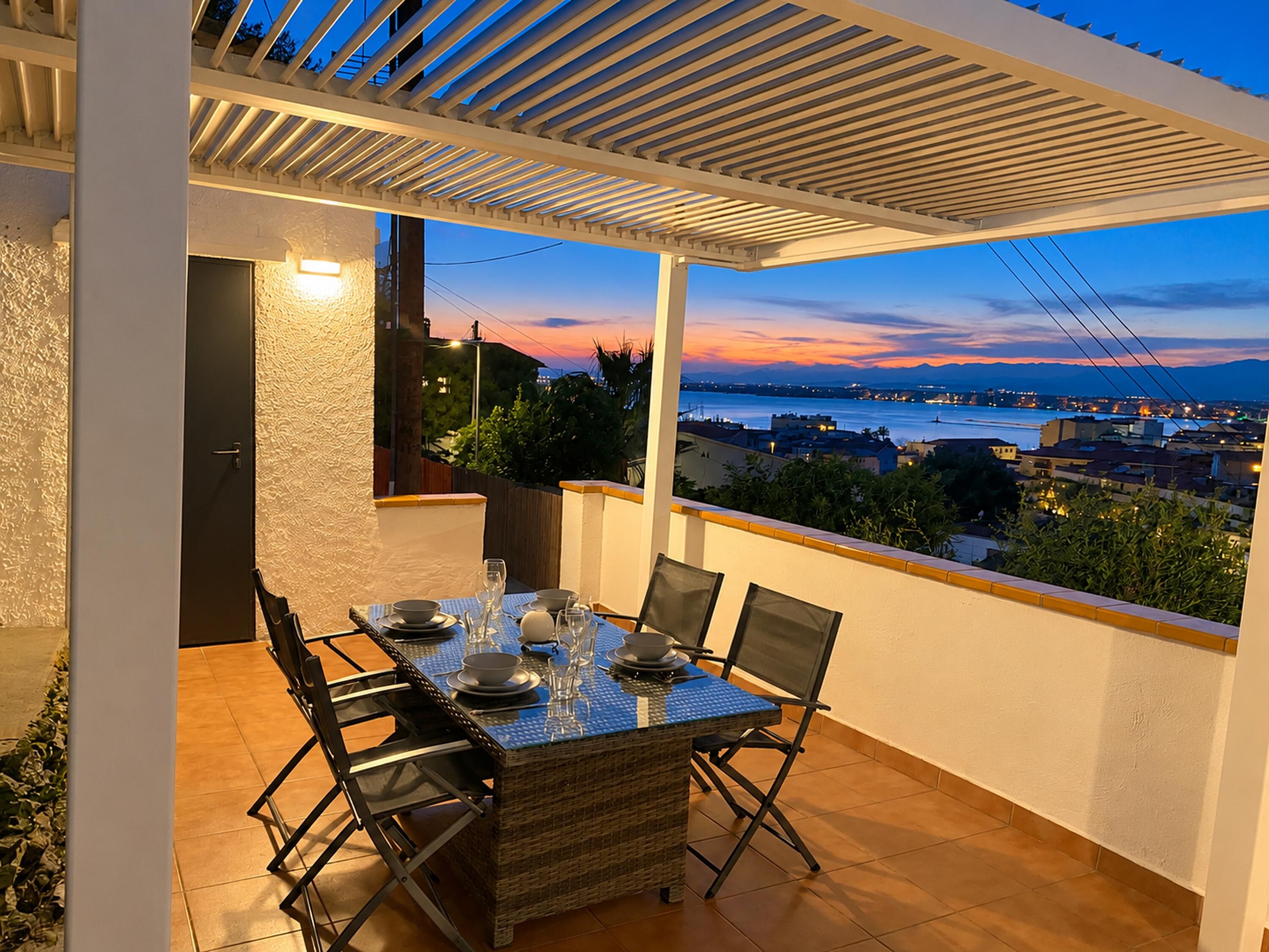 An outdoor dining area with a table set for two, overlooking a cityscape and water.