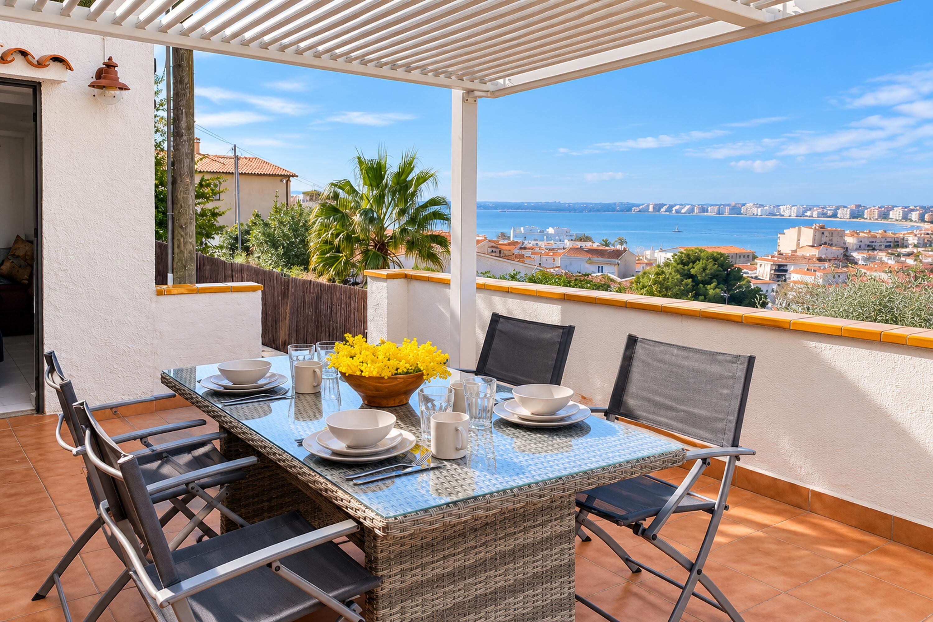 A covered outdoor dining area with a table set for two, overlooking a coastal cityscape.
