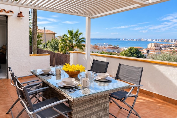 A covered outdoor dining area with a table set for two, overlooking a coastal cityscape.