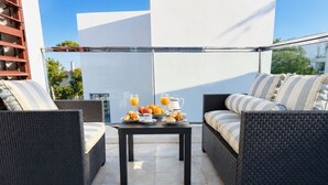 Un balcón con mobiliario de mimbre, una mesa con alimentos para el desayuno y una vista despejada del cielo.
