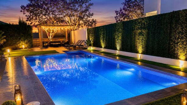 Una piscina rectangular con borde de azulejos, rodeada por un césped cuidado y un seto.