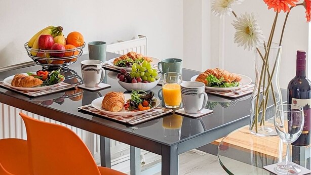 Een ontbijttafel met croissants, fruit, sap, een vaas met bloemen en een wijnfles.