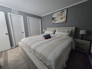 A bedroom with a bed, a nightstand, a lamp, and a door.