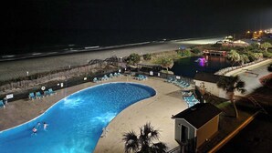 Une piscine avec des chaises longues et une vue sur la plage la nuit.