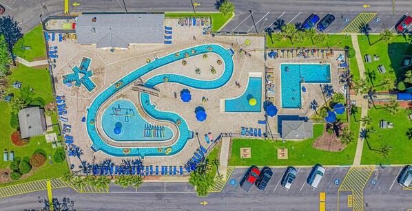 An aerial view of a swimming pool complex with multiple pools, sun loungers, and a parking area.