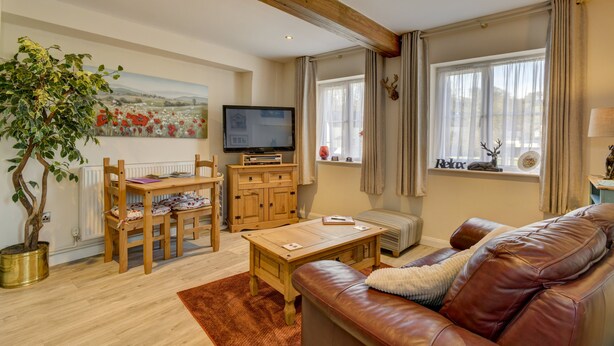 A living room with a wooden dining table, a leather sofa, a television, and a large window with curtains. - The Old Post Office, Exford (Exford)