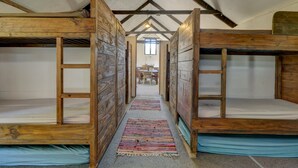 Une pièce avec des lits superposés, un plafond en bois et un couloir central menant à un espace repas.