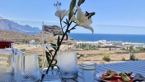 Un tavolo imbandito con un pasto, un bicchiere d'acqua e un'elegante composizione floreale, con vista sul mare e sulle montagne.