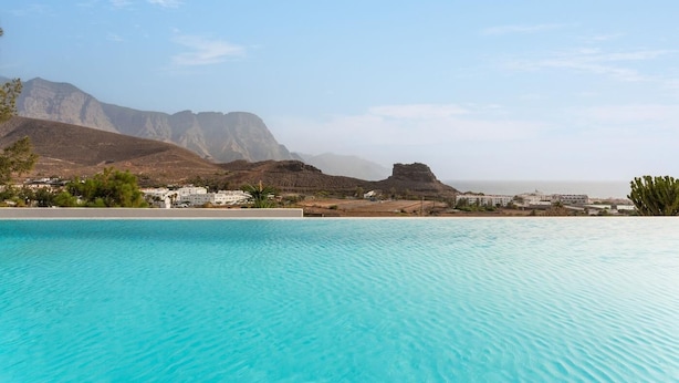 Una piscina con acqua cristallina, circondata da edifici e montagne sullo sfondo.
