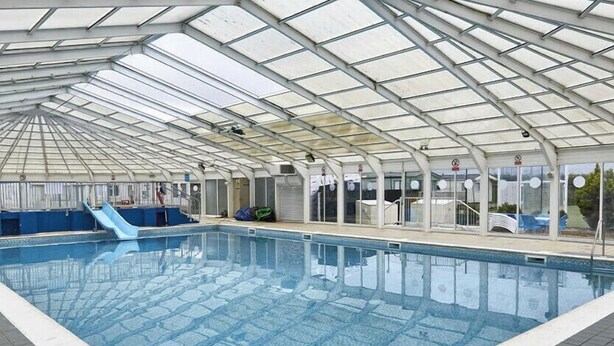 An indoor swimming pool with a glass ceiling, a slide, and a tiled floor.