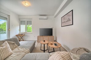 A living room with a sofa, a coffee table, a TV, and a small wooden table with a plant. - A 2 spacious apt w big balcony,4 min walk to beach (Split)