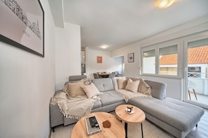 A modern living room with a grey sectional sofa, a round wooden coffee table, and a framed cityscape picture on the wall. - A 2 spacious apt w big balcony,4 min walk to beach (Split)