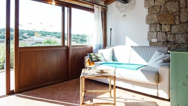 A room with a wooden ceiling, a stone wall, a white sofa with a blue throw, and a small table with a vase and a book. - Detached Villa in the most quiet and reserved area (Santa Teresa di Gallura)