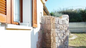 A stone wall with a metal gate, a window with wooden shutters, and a tiled patio area. - Detached Villa in the most quiet and reserved area (Santa Teresa di Gallura)