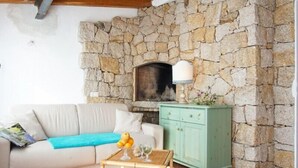 A cozy living room with a stone wall, a fireplace, a green cabinet, and a white sofa. - Detached Villa in the most quiet and reserved area (Santa Teresa di Gallura)