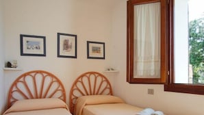 A room with two single beds, each with a headboard, a window with a curtain, and three framed pictures on the wall. - Detached Villa in the most quiet and reserved area (Santa Teresa di Gallura)