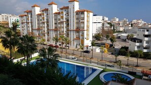 A modern hotel with a pool area, featuring multiple balconies and a view of the surrounding cityscape. - Beautiful 2-Bed Apartment in Estepona Port (Estepona)