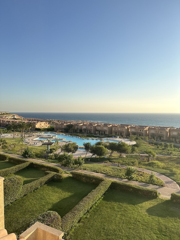 A resort with a large swimming pool, well-maintained lawns, and a view of the sea.