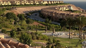 A coastal resort with terraced buildings, a parking area, and a landscaped garden with palm trees.