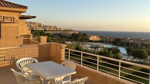 A terrace with a table and chairs, overlooking a pool and buildings.