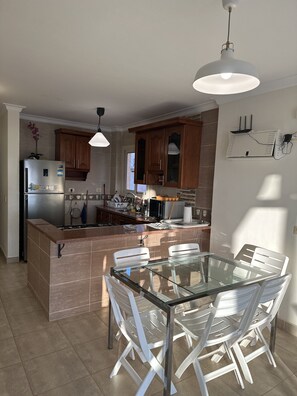 A modern kitchen with a central island, white chairs, and a glass table.