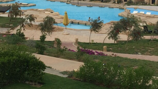 A resort with multiple swimming pools, a view of the ocean, and a large building with a tiled roof.