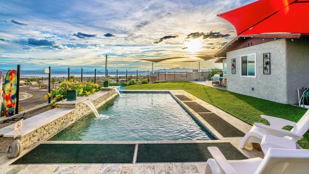 Una piscina con caída de agua, rodeada de un césped cuidado y una pérgola roja.
